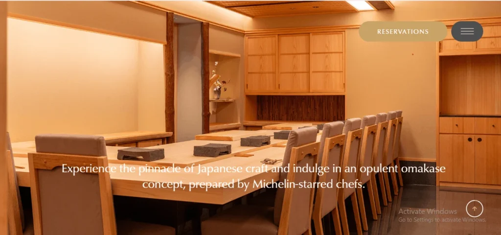 Website screenshot of a luxury Japanese Sushi Sakuta restaurant dining room with a wooden counter and minimalist interior design.