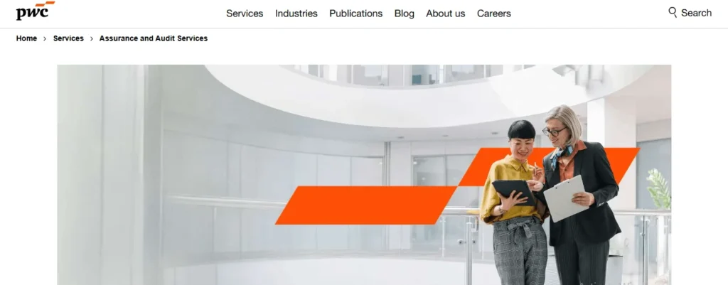 Screenshot of the PwC website's "Assurance and Audit Services" page. The website header includes the PwC logo on the left and navigation menu links for Services, Industries, Publications, Blog, About us, and Careers on the right, alongside a search button. Below the navigation, breadcrumb links show "Home > Services > Assurance and Audit Services." The primary banner image features two professional women standing in a bright, modern office courtyard with white circular architecture. The woman on the left holds a tablet while the woman on the right holds a clipboard, both looking down at the tablet screen. A large, stylistic orange graphic overlay is positioned next to them.