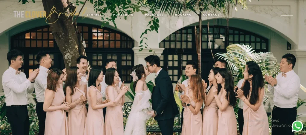 Website banner for The Clover Bridal, featuring a newlywed bride and groom kissing, surrounded by clapping bridesmaids in blush pink dresses and groomsmen in white shirts and bow ties.