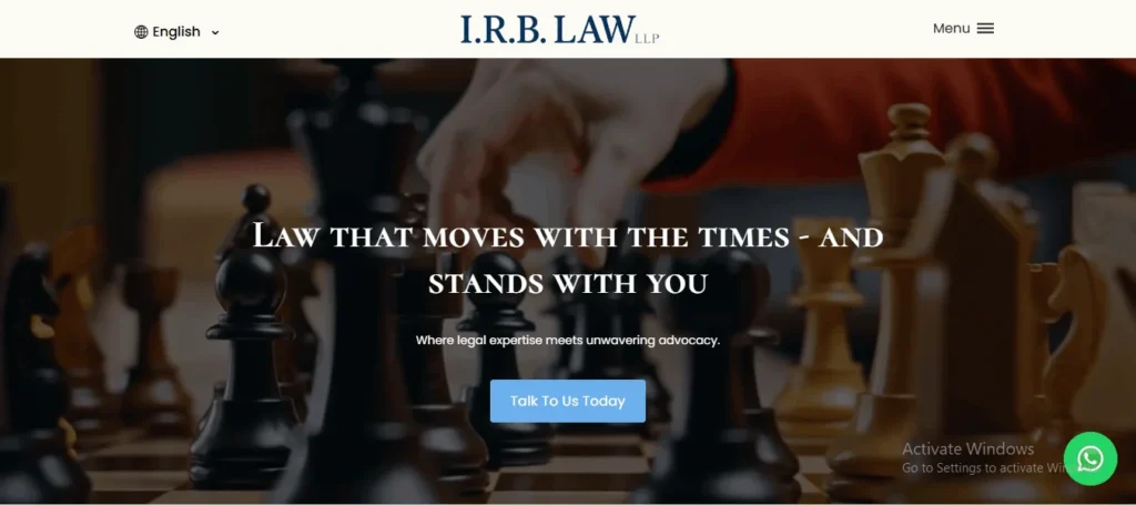 A screenshot of the I.R.B. LAW LLP website homepage, featuring a dark background image of a person’s hand moving a chess piece on a chessboard. Overlaid text reads "LAW THAT MOVES WITH THE TIMES - AND STANDS WITH YOU" followed by the tagline "Where legal expertise meets unwavering advocacy." A light blue button in the center says "Talk To Us Today." The clean white header displays the firm's name, "I.R.B. LAW LLP," alongside an English language selector on the left and a hamburger menu icon on the right. A green WhatsApp chat icon is visible in the bottom right corner.