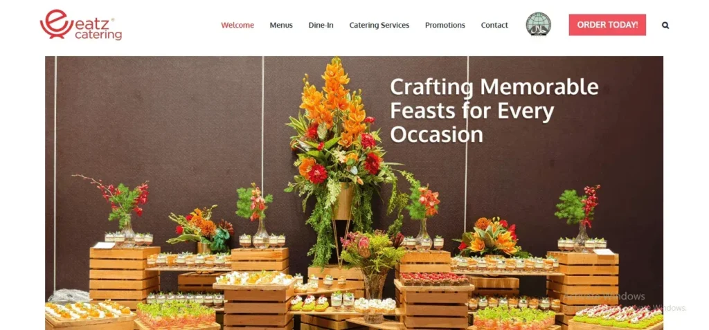 Eatz Catering banner showing a buffet setup with finger foods on wooden crates, vibrant orange floral centerpieces, and the text "Crafting Memorable Feasts for Every Occasion."