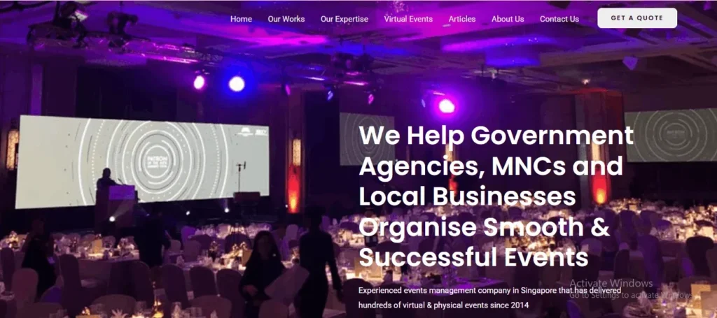 Website homepage banner featuring a dimly lit, large-scale event hall with round banquet tables set under purple and blue stage lighting. A speaker stands at a podium next to a wide projection screen showing a circular graphic. Overlay text reads: "We Help Government Agencies, MNCs and Local Businesses Organise Smooth & Successful Events."