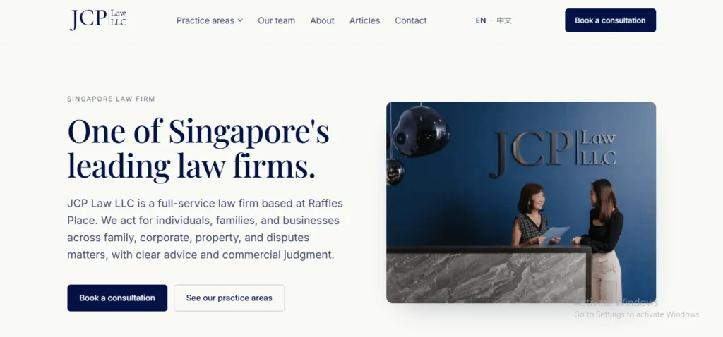 Screenshot of the homepage for "JCP Law LLC", a Singapore law firm. The top navigation bar displays the company logo on the left, menu links for "Practice areas", "Our team", "About", "Articles", and "Contact", language toggles ("EN", "中文"), and a dark blue "Book a consultation" button. The main section features bold text reading "One of Singapore's leading law firms.", followed by a description stating that JCP Law LLC is a full-service firm based at Raffles Place serving individuals, families, and businesses. Two action buttons, "Book a consultation" and "See our practice areas", sit below the text. On the right, a photograph shows two female legal professionals talking behind a reception desk set against a dark blue wall featuring the "JCP Law LLC" logo.