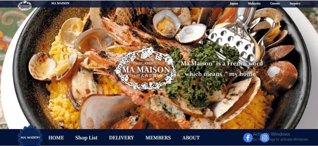 Website banner for Ma Maison restaurant featuring a close-up of a seafood paella dish with prawns, clams, and mussels over yellow rice. Overlaid text reads, 'Singapore Ma Maison. "Ma Maison" is a French word which means "my home."