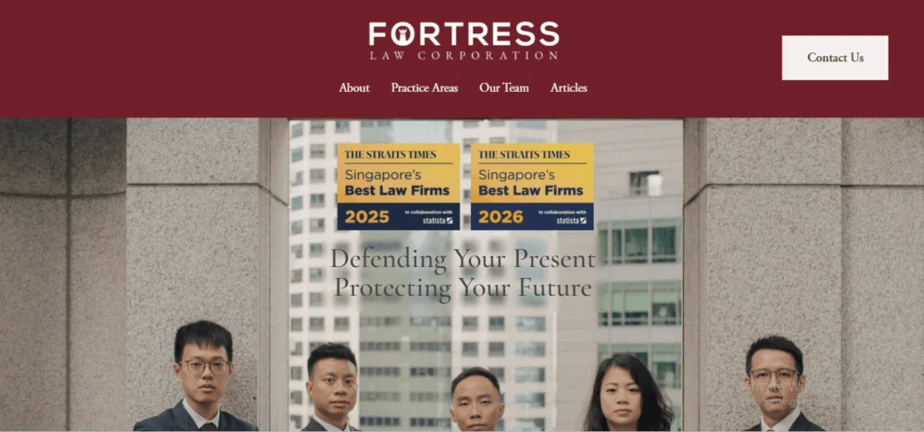 A screenshot of the Fortress Law Corporation website homepage, displaying a maroon header with the white and maroon logo: “FORTRESS LAW CORPORATION.” Below the logo are links for “About,” “Practice Areas,” “Our Team,” and “Articles,” alongside a white “Contact Us” button in the top-right corner. The main section features a photograph with the blurry building in the background of four lawyers from their torso up, standing in a professional pose. At the top of the photo are two award badges titled “THE STRAITS TIMES” and “Singapore’s Best Law Firms.” The badge on the left reads “2025” with “In collaboration with statista” below. The badge on the right is almost identical, with the title but reading “2026.” The large black and white centered text overlay in front of the four lawyers states: “Defending Your Present, Protecting Your Future.”