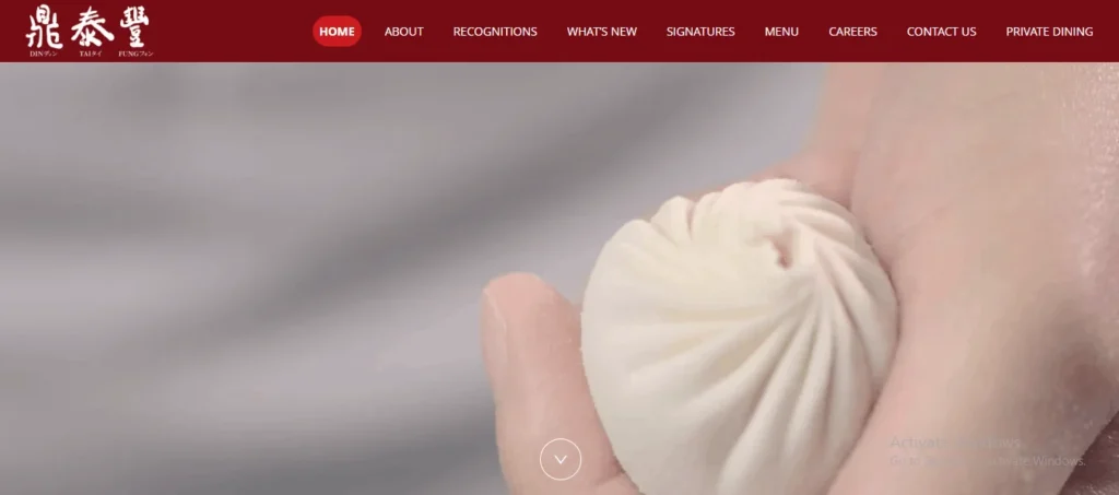 "Website homepage for Din Tai Fung featuring a dark red navigation header with the restaurant's logo in white on the far left. The main banner displays a close-up, detailed view of a person's hands carefully shaping a single, intricately pleated xiao long bao (soup dumpling) against a soft, out-of-focus background."